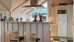Une cuisine avec des meubles en bois, un réfrigérateur blanc et un coin bar avec deux chaises.