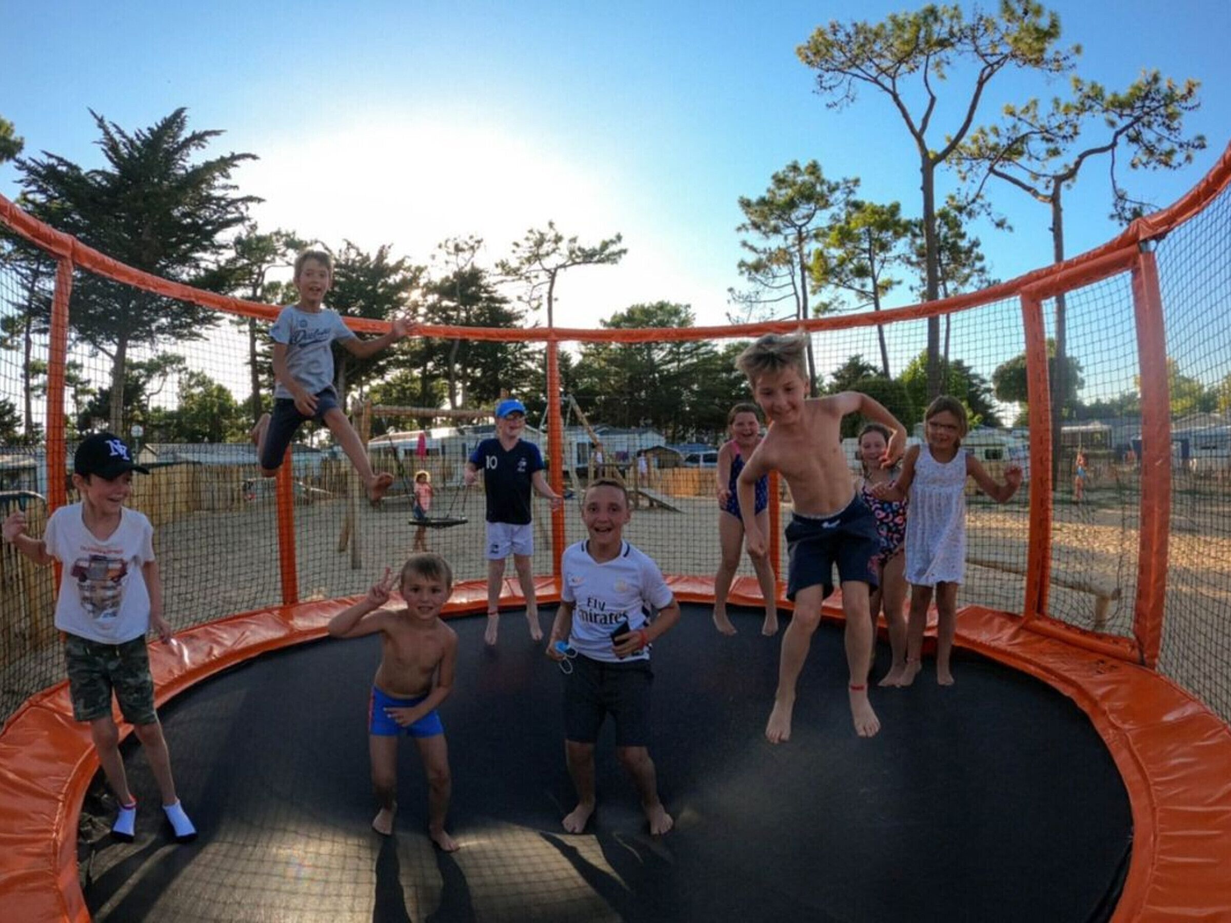 Eine Gruppe Kinder spielt auf einem Trampolin, das von einem Sicherheitsnetz umgeben ist.