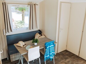 Ein kleines Zimmer mit Fenster, Tisch, Stuhl, Sitzbank und Tür.
