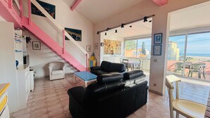 Ein Wohnzimmer mit einer schwarzen Ledersofa, einem weißen Sessel, einem blauen Couchtisch und einer Treppe mit rosafarbenen Geländern.