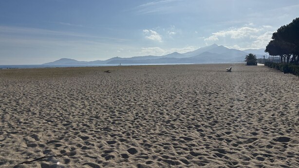 Ein weiter Sandstrand mit Fußabdrücken, einem klaren Himmel und fernen Bergen.