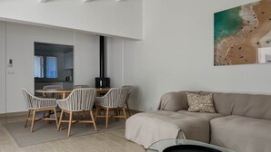 A modern living room with a sofa, a dining table with chairs, a fireplace, and a wall-mounted artwork. - Renovated Villa in La Palmyre - Sleeps 6 - Air Conditioning - Wifi - Parking (La Palmyre)