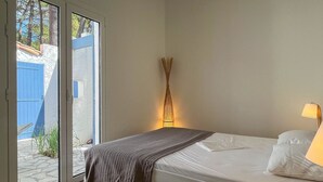 A bedroom with a bed, a bedside lamp, and a view through a sliding door to an outdoor area. - Renovated Villa in La Palmyre - Sleeps 6 - Air Conditioning - Wifi - Parking (La Palmyre)