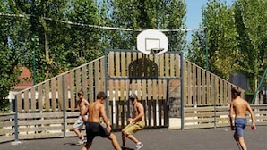 Una cancha de baloncesto con valla de madera y árboles al fondo.