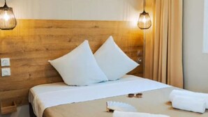 Habitación de hotel con cabecera de madera, dos lámparas de noche, cama con ropa blanca, dos almohadas, un par de gafas de sol y una toalla doblada sobre la cama.