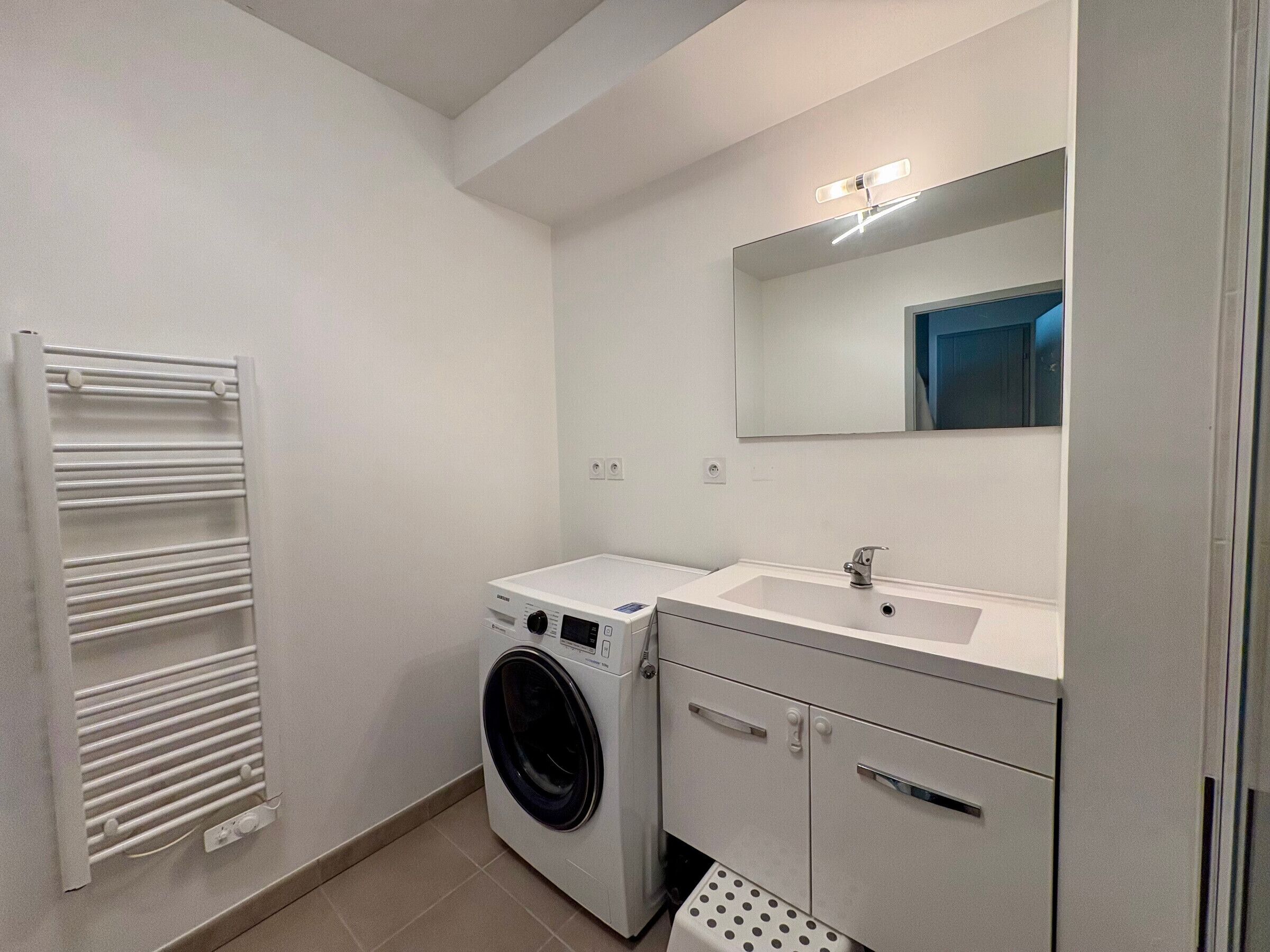 Un bagno compatto e moderno dotato di lavatrice e asciugatrice integrate, un lavandino e uno specchio sopra.