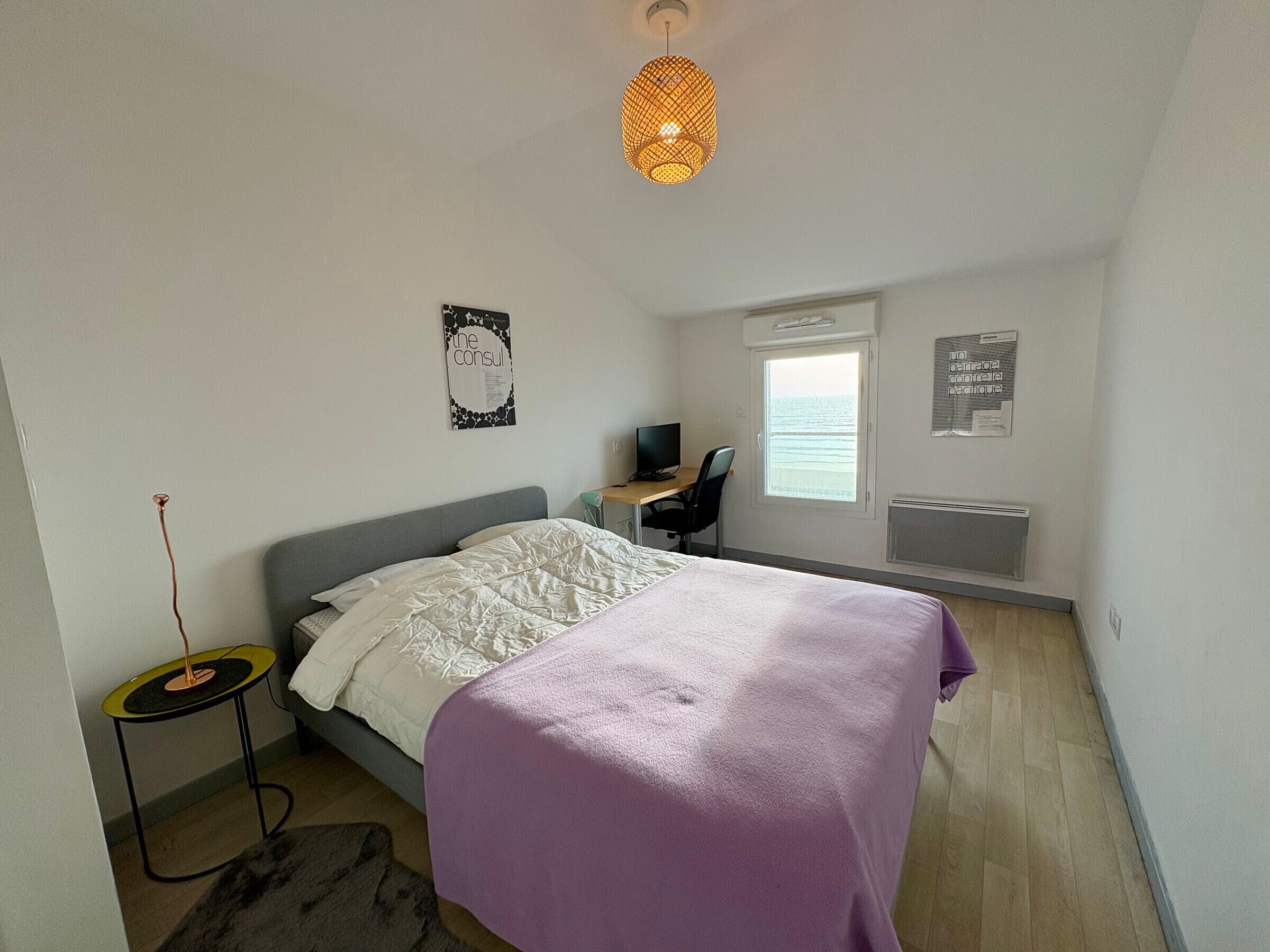 Ein Schlafzimmer mit Bett, Schreibtisch, Stuhl, Fenster und Heizkörper.