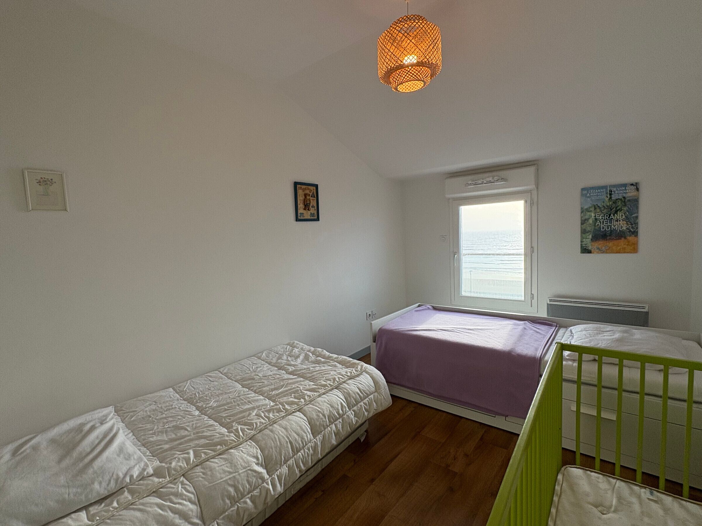 A bedroom with two beds, a window with a view, a hanging light fixture, and a painting on the wall.