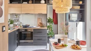 A modern kitchen with wooden cabinets, a built-in oven, and a dining area with a table set for a meal. - Mobile Home 34m² with Terrace - 2 Bedrooms, Sleeps 4 (Saint-Jean-de-Monts)