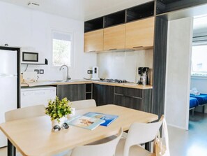 A modern kitchen with a dining area, featuring a built-in stove, microwave, and sink. - Mobile Home 34m² with Terrace - 2 Bedrooms, Sleeps 4 (Saint-Jean-de-Monts)