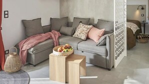 A modern living room with a grey sectional sofa, a small wooden side table with a fruit bowl, and a woven basket. - Mobile Home 34m² with Terrace - 2 Bedrooms, Sleeps 4 (Saint-Jean-de-Monts)