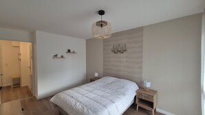 Een slaapkamer met een groot bed, een nachtkastje met een lamp, een wandlamp en een deur naar een badkamer.