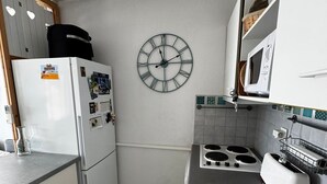 Kompakti keittiö, jossa on jääkaappi, liesi, mikroaaltouuni ja seinäkello.