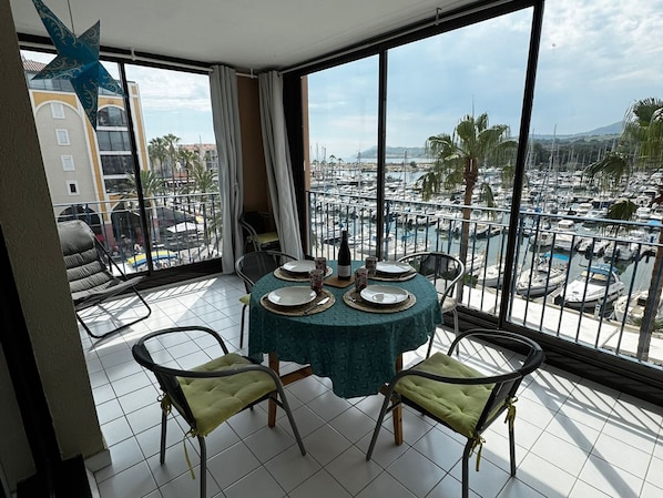 A balcony with a table set for dining, overlooking a marina with boats and palm trees.