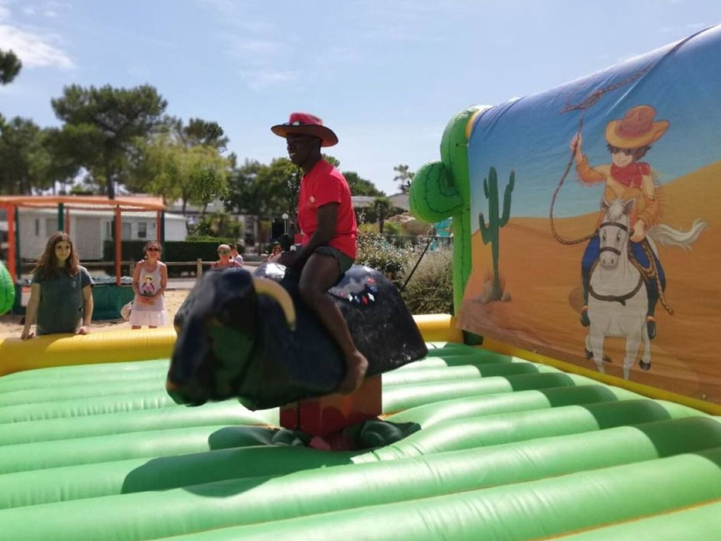 Una persona montando un caballo inflable en un área de juegos al aire libre, con un mural de un vaquero a caballo.
