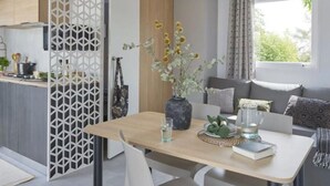 A modern living room with a wooden dining table, a sofa, and a decorative vase with flowers. - Mobile home for 4 in Saint-Jean-de-Monts (Saint-Jean-de-Monts)