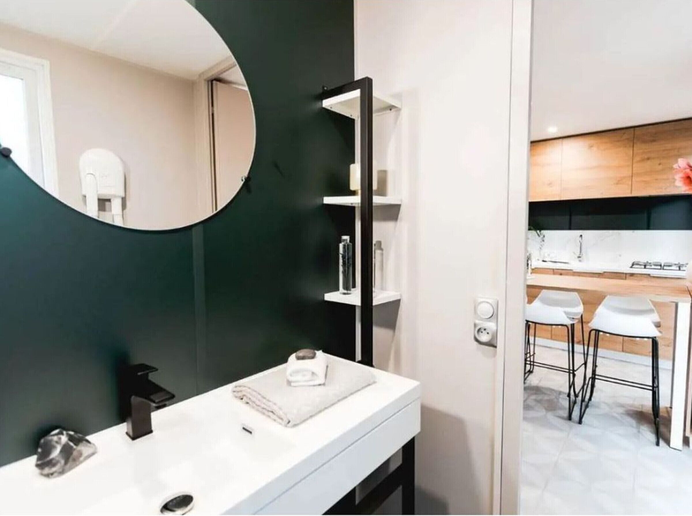 A modern bathroom with a white vanity, a round mirror, and a dark green accent wall.