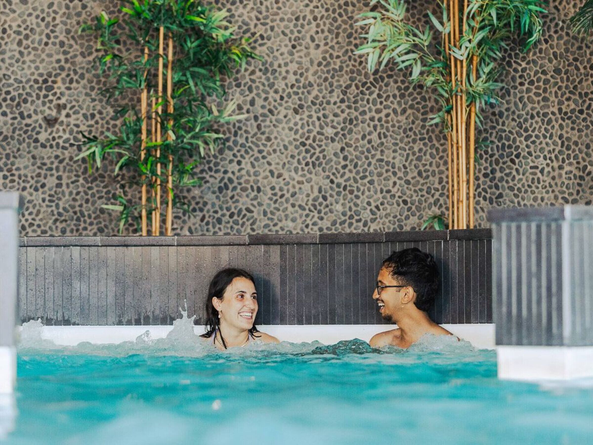 A swimming pool with a textured stone wall and bamboo plants.
