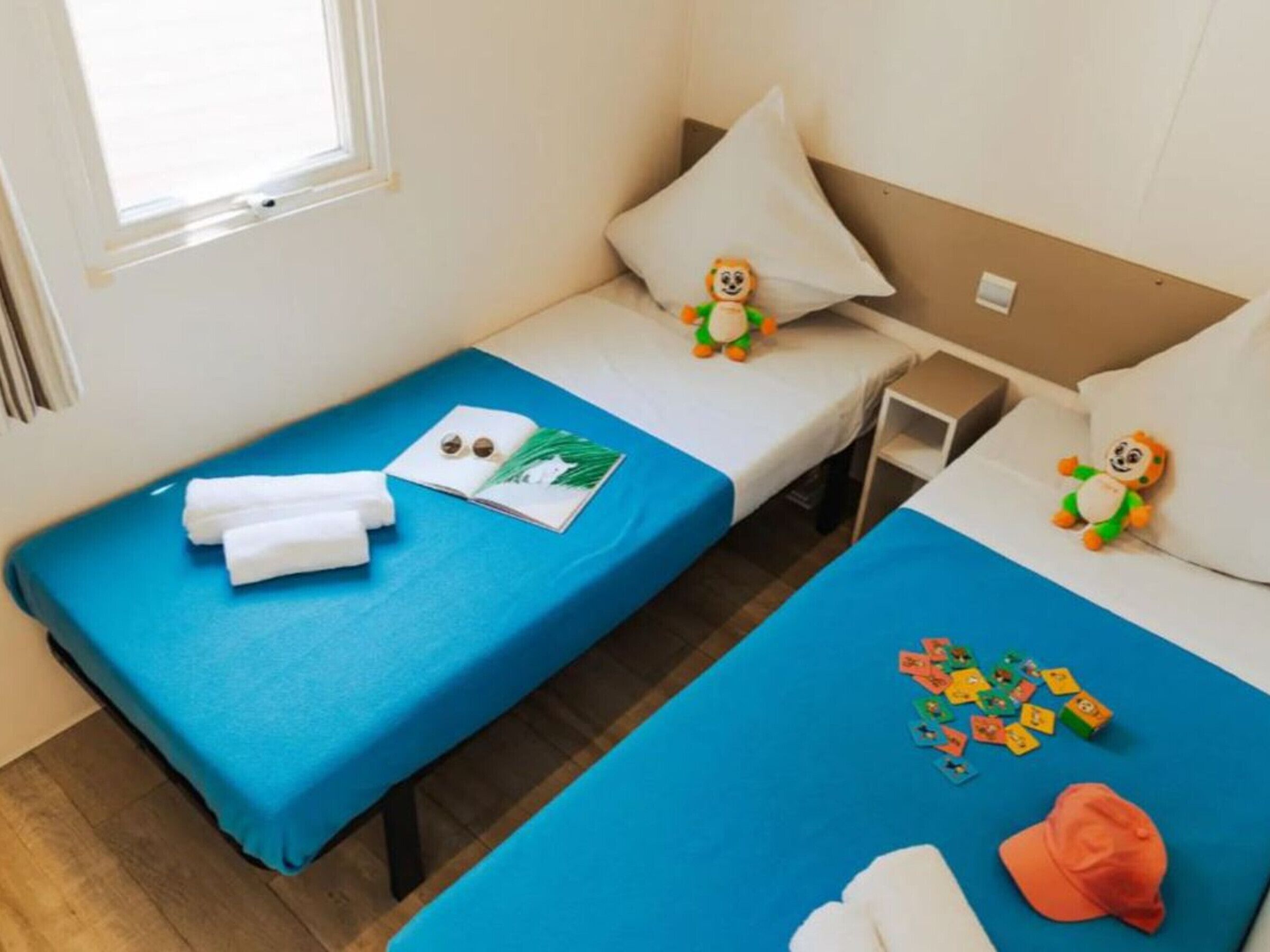 Una camera d'albergo con due letti singoli, ognuno con copriletto e cuscini blu. C'è un tavolino con un libro e un paio di orecchini sopra.
