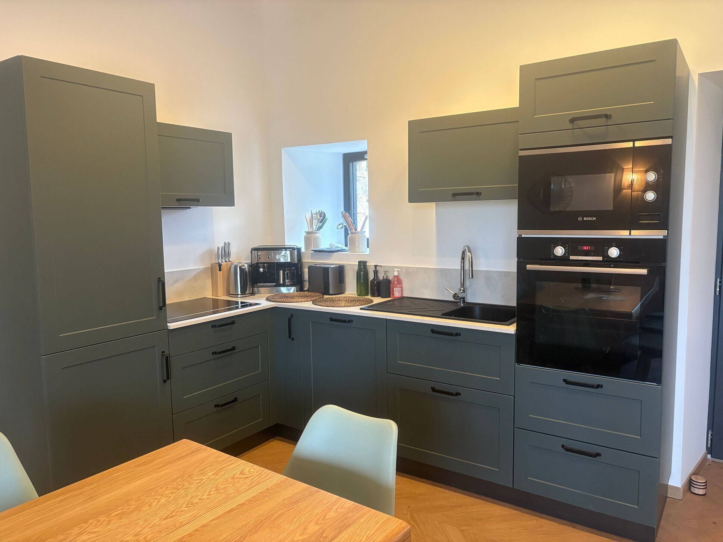 Eine moderne Küche mit grauen Schränken, einem Bosch-Backofen, einer Kaffeemaschine und einem Spülbecken.