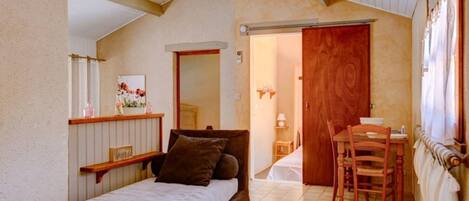 A bedroom with a bed, a wooden door, a small table with chairs, and a mirror.