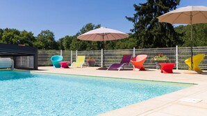 Una piscina con sillas de descanso coloridas y sombrillas, rodeada por una valla y árboles.