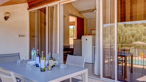Un área de comedor al aire libre con mesa y sillas, un refrigerador y vistas a una piscina y jardín.