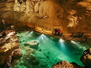 Une grotte avec une piscine, des rampes de protection en bois et des stalactites.