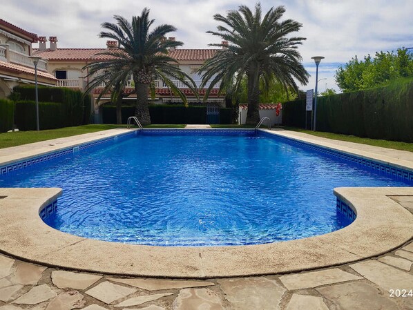 Ein rechteckiger Swimmingpool mit Steinrand, umgeben von einem gepflegten Rasen und Palmen.