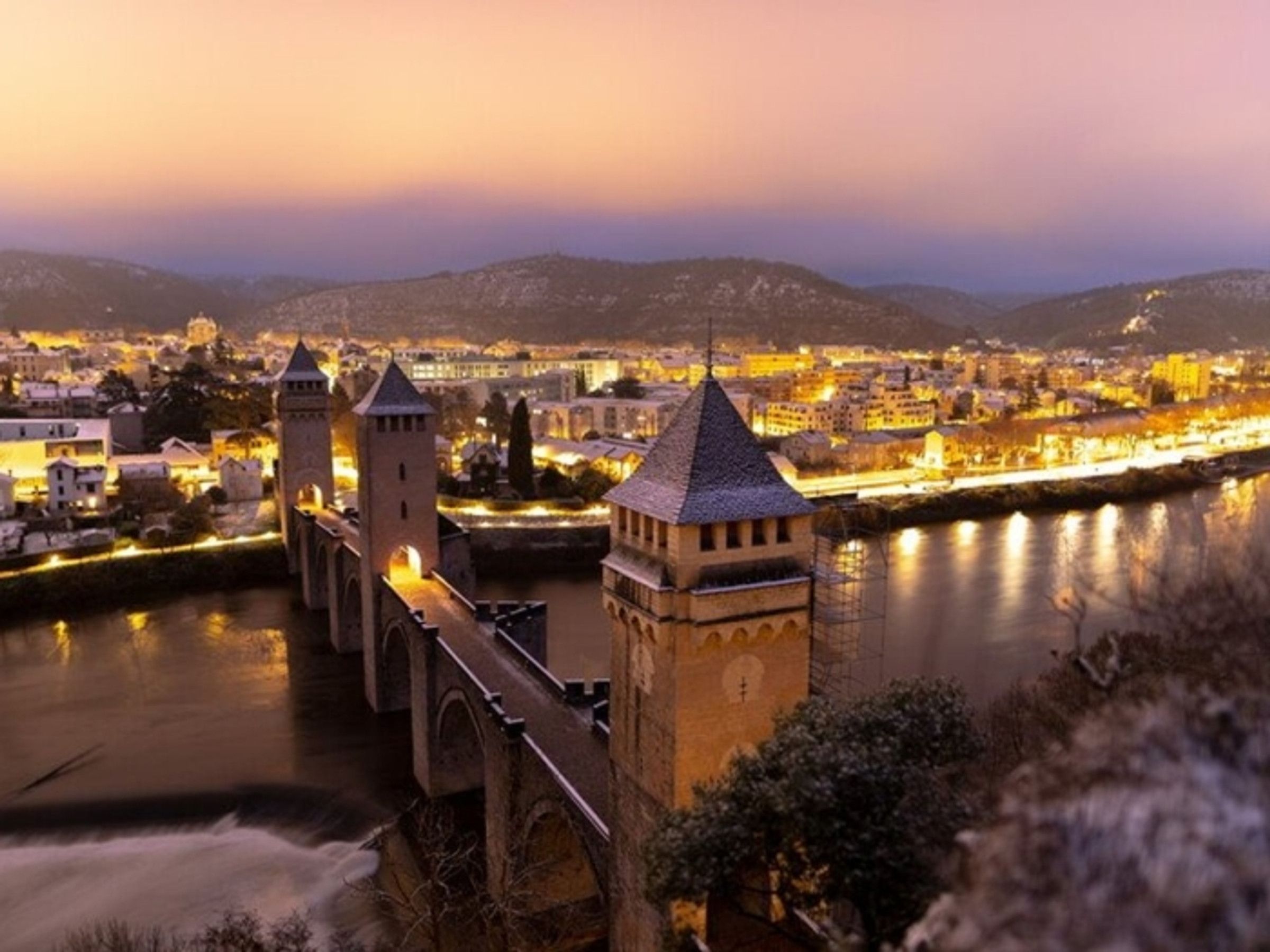 Un pont historique, doté de tours, surplombant une rivière, avec une vue sur la ville au crépuscule.