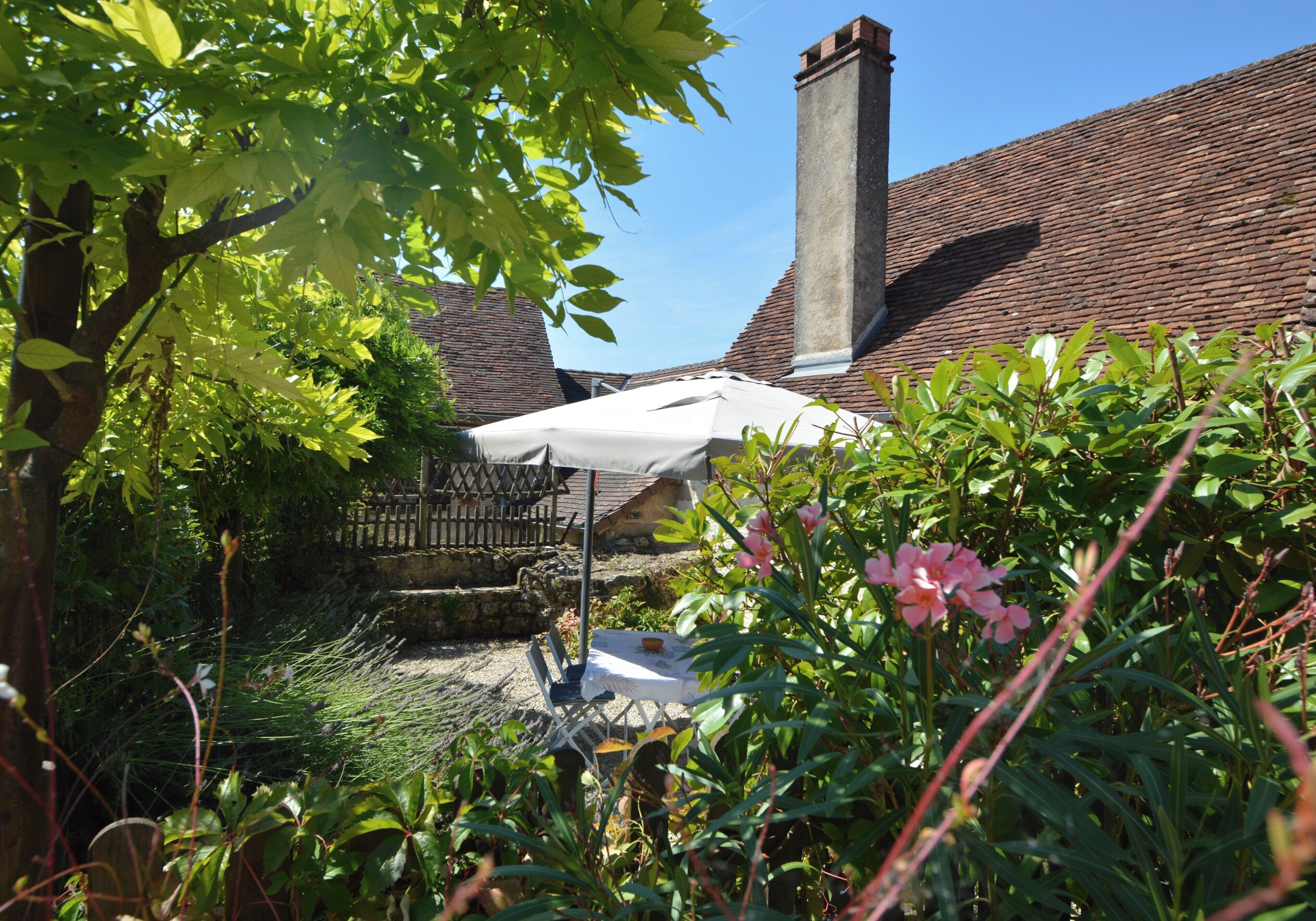 A garden area with a white umbrella, a stone bench, and a brick chimney.