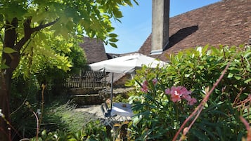 A garden area with a white umbrella, a stone bench, and a brick chimney.