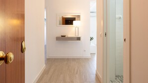 Een gang met een houten deur, een spiegel, een lamp en een douchedeur van glas.