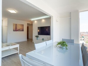 A modern living room with a glass table, white furniture, a flat-screen TV, and a painting of a bridge. - Spacious apartment in the heart of Rincón de la Victoria (Rincón de la Victoria)