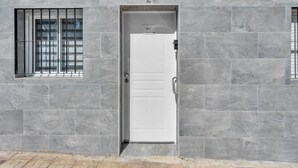 A modern building facade with a white door, large windows with metal bars, and grey stone tiles. - Modern Apartment in Málaga (Málaga)