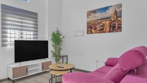 A modern living room with a flat-screen TV, a pink sofa, a small round table with a plant, and a cityscape painting on the wall. - Modern Apartment in Málaga (Málaga)