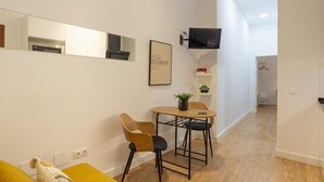 Un salon moderne avec un canapé, une petite table et deux chaises, un téléviseur fixé au mur et un tableau encadré.