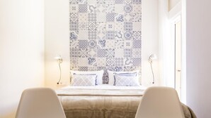 Una camera d'albergo con un letto, due sedie, un tavolino con un vaso e una parete decorata.