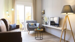 Un soggiorno moderno con divano, poltrona, televisore, lampada da terra e un tavolino con fiori.