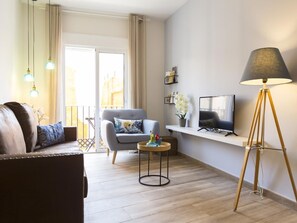 A modern living room with a sofa, armchair, TV, floor lamp, and a small table with flowers. - Elegant apartment in Malaga city center, close to the beach (Málaga)
