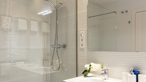 Un bagno moderno con box doccia in vetro, un lavandino bianco con specchio e un vaso di fiori bianchi.