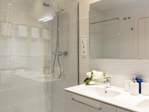 A modern bathroom with a glass shower enclosure, a white sink with a mirror, and a vase of white flowers. - Elegant apartment in Malaga city center, close to the beach (Málaga)