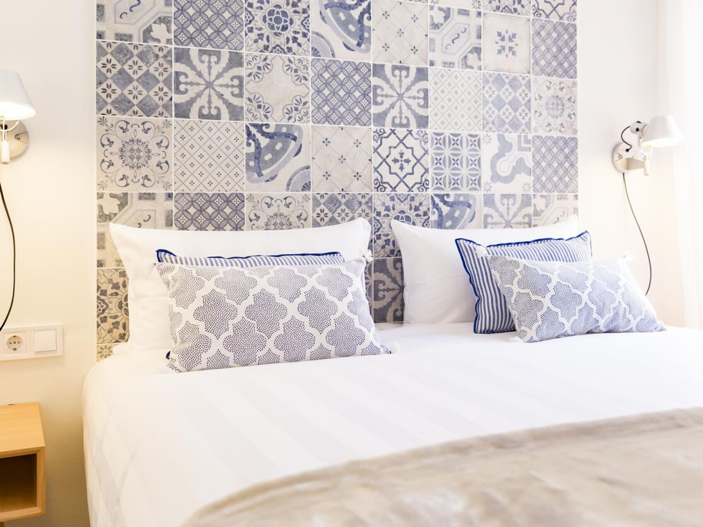 A bed with patterned pillows, a tiled wall, and bedside lamps.