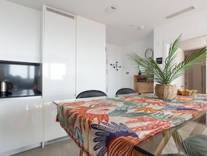 A modern kitchen with white cabinets, a stainless steel kettle, and a table with a colorful tablecloth. - Modern apartment on the 26th floor with common areas in Málaga (Málaga)