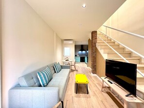 En moderne stue med sofa, et lille bord, et fjernsyn og en trappe, der fører til en etage ovenover.