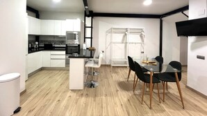 Cozinha moderna com armários brancos, bancada preta e área de refeições com mesa de vidro e cadeiras pretas.