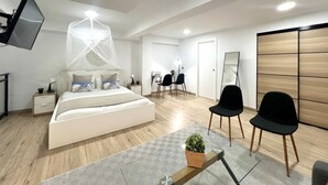 Um quarto moderno com cama, mesas de cabeceira, escrivaninha, cadeiras, um espelho grande e uma TV fixada na parede.