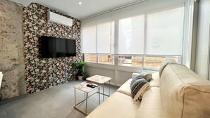 A modern living room with a beige sofa, a small coffee table, and a flat-screen TV mounted on a floral-patterned wall. - Bright apartment at Malagueta beach with private terrace (Málaga)