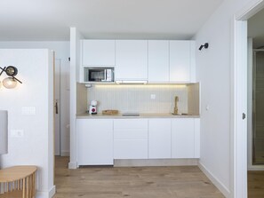 Eine kompakte Küche mit weißen Schränken, einer Mikrowelle, einer Kaffeemaschine und einem kleinen Holztisch.