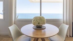 Ein runder Tisch mit einer Blumenvase, zwei Stühlen und Meerblick durch große Fenster.